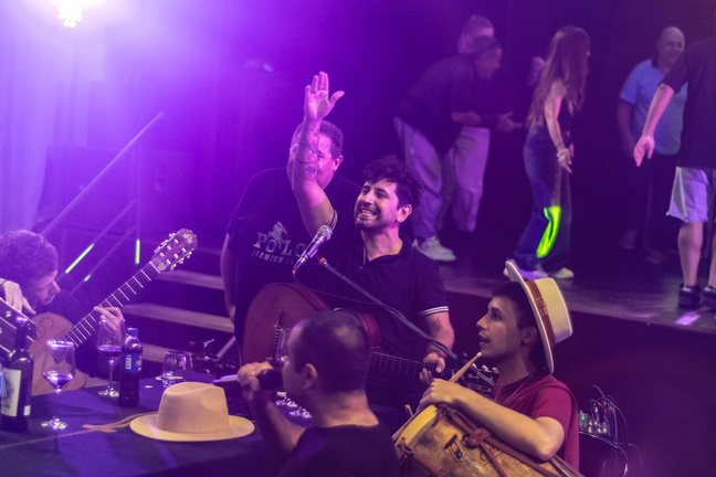 Músicos y público en la sala con luces violetas